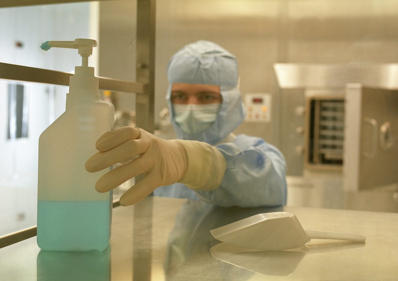A scientist in protective gear reaching for a sanitizer bottle in a laboratory setting.